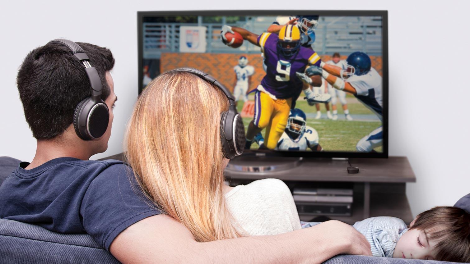 man and woman with headphones watching football game on TV